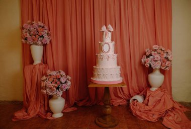 İzole edilmiş çiçek aranjmanları ve romantik kutlamalar için örtülü kumaşlarla sergilenen lüks pembe düğün pastası..