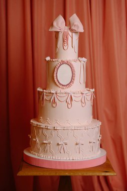 Şatafatlı pembe katlı pasta, fiyonklu ve süslü detaylar, düğünler ve özel kutlamalar için mükemmel..