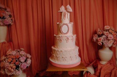 Çiçek vazoları ile çevrili süslü pembe katlı pasta, kutlamalar için mükemmel..