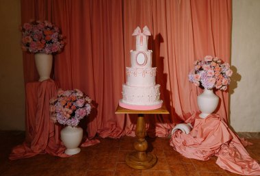 İzole edilmiş çiçek aranjmanları ve romantik kutlamalar için örtülü kumaşlarla sergilenen lüks pembe düğün pastası..