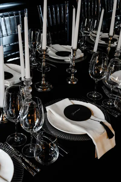 Siyah temalı lüks resmi yemek masası, cam eşyalar, gümüş şamdanlar ve sofistike yer ayarları..