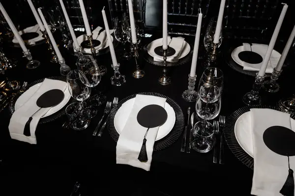 Resmi bir etkinlik için mumlar, cam eşyalar ve peçetelerle süslü lüks siyah beyaz masa..