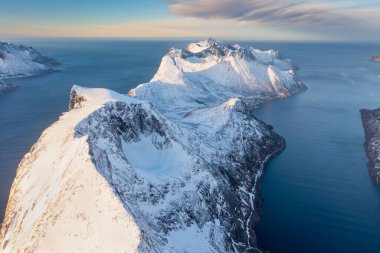 Snow covered mountain range on coastline in winter, Norway. Senja panoramic aerial view landscape nordic snow cold winter norway ocean cloudy sky snowy mountains. Troms county, Fjordgard