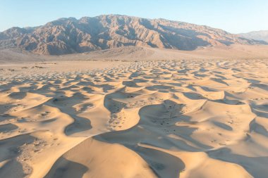 Mesquite Düzlüğü Kum Tepesi 'nde, Kaliforniya' daki Ölüm Vadisi Ulusal Parkı 'nda güneş doğarken oluşan doğal dalgalı kum deseni manzarası. Mojave çölünde sabah yürüyüşü Amargosa sıradağları arkada.