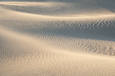 Mesquite Düzlüğü Kum Tepesi 'nde, Kaliforniya' daki Ölüm Vadisi Ulusal Parkı 'nda güneş doğarken oluşan doğal dalgalı kum deseni manzarası. Mojave çölünde sabah yürüyüşü Amargosa sıradağları arkada.