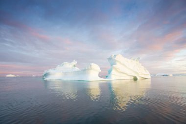 Antarktika 'da buzdağları olan kutup doğası. Ufukta gece yarısı güneş batarken gün batarken. Yaz Gecesi Güneşi ve buzdağları. Buz üzerinde büyük mavi buz. İklim değişikliği küresel ısınma.