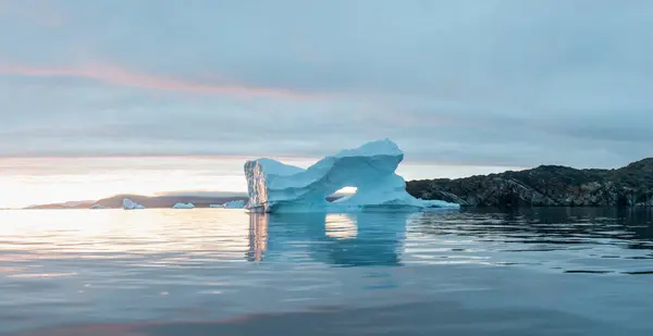 Arctic nature landscape with icebergs in Antarctica with midnight sun sunset sunrise in the horizon. Summer Midnight Sun and icebergs. Big blue ice in icefjord. Climate change global warming.