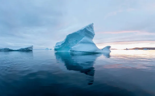 Arctic nature landscape with icebergs in Antarctica with midnight sun sunset sunrise in the horizon. Summer Midnight Sun and icebergs. Big blue ice in icefjord. Climate change global warming.
