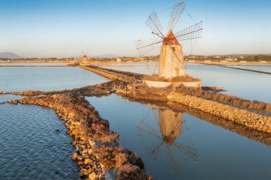 Marsala, Sicilya adası, İtalya 'nın Trapani tuz düzlüklerinde ve Sicilya' nın eski yel değirmeninde tuz buharlaştırma göletinde gün batımı. Güneşli ve güzel bir günde.