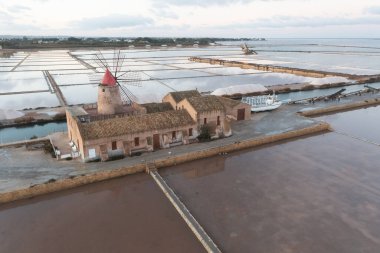 Marsala, Sicilya adası, İtalya 'nın Trapani tuz düzlüklerinde ve Sicilya' nın eski yel değirmeninde tuz buharlaştırma göletinde gün batımı. Güneşli ve güzel bir günde.