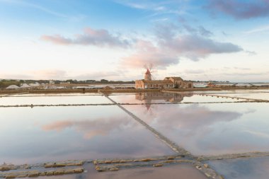 Marsala, Sicilya adası, İtalya 'nın Trapani tuz düzlüklerinde ve Sicilya' nın eski yel değirmeninde tuz buharlaştırma göletinde gün batımı. Güneşli ve güzel bir günde.