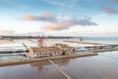 Marsala, Sicilya adası, İtalya 'nın Trapani tuz düzlüklerinde ve Sicilya' nın eski yel değirmeninde tuz buharlaştırma göletinde gün batımı. Güneşli ve güzel bir günde.