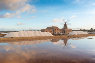 Marsala, Sicilya adası, İtalya 'nın Trapani tuz düzlüklerinde ve Sicilya' nın eski yel değirmeninde tuz buharlaştırma göletinde gün batımı. Güneşli ve güzel bir günde.