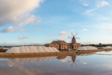Marsala, Sicilya adası, İtalya 'nın Trapani tuz düzlüklerinde ve Sicilya' nın eski yel değirmeninde tuz buharlaştırma göletinde gün batımı. Güneşli ve güzel bir günde.