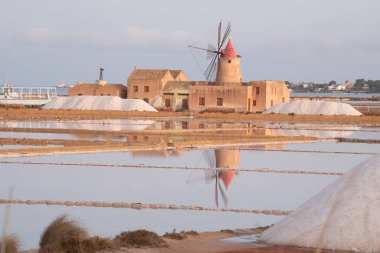 Marsala, Sicilya adası, İtalya 'nın Trapani tuz düzlüklerinde ve Sicilya' nın eski yel değirmeninde tuz buharlaştırma göletinde gün batımı. Güneşli ve güzel bir günde.