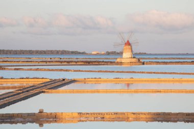 Marsala, Sicilya adası, İtalya 'nın Trapani tuz düzlüklerinde ve Sicilya' nın eski yel değirmeninde tuz buharlaştırma göletinde gün batımı. Güneşli ve güzel bir günde.