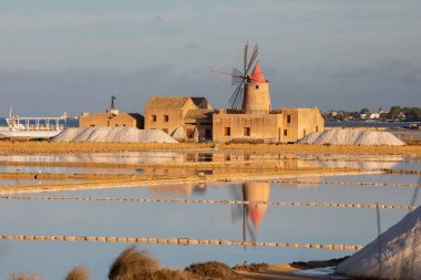 Marsala, Sicilya adası, İtalya 'nın Trapani tuz düzlüklerinde ve Sicilya' nın eski yel değirmeninde tuz buharlaştırma göletinde gün batımı. Güneşli ve güzel bir günde.