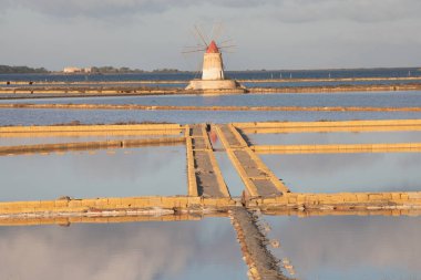 Marsala, Sicilya adası, İtalya 'nın Trapani tuz düzlüklerinde ve Sicilya' nın eski yel değirmeninde tuz buharlaştırma göletinde gün batımı. Güneşli ve güzel bir günde.