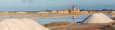 Marsala, Sicilya adası, İtalya 'nın Trapani tuz düzlüklerinde ve Sicilya' nın eski yel değirmeninde tuz buharlaştırma göletinde gün batımı. Güneşli ve güzel bir günde.