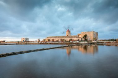 Marsala, Sicilya adası, İtalya 'nın Trapani tuz düzlüklerinde ve Sicilya' nın eski yel değirmeninde tuz buharlaştırma göletinde gün batımı. Güneşli ve güzel bir günde.