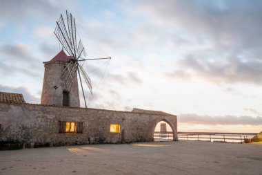 Marsala, Sicilya adası, İtalya 'nın Trapani tuz düzlüklerinde ve Sicilya' nın eski yel değirmeninde tuz buharlaştırma göletinde gün batımı. Güneşli ve güzel bir günde.