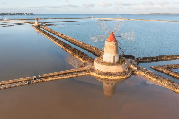 Marsala, Sicilya adası, İtalya 'nın Trapani tuz düzlüklerinde ve Sicilya' nın eski yel değirmeninde tuz buharlaştırma göletinde gün batımı. Güneşli ve güzel bir günde.