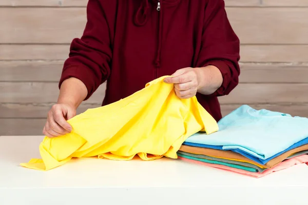 stock image A woman folds several multi-colored t-shirts. Preparing clothes for donation to charity. Conscious consumption. Disposal of unused clothing. slow fashion