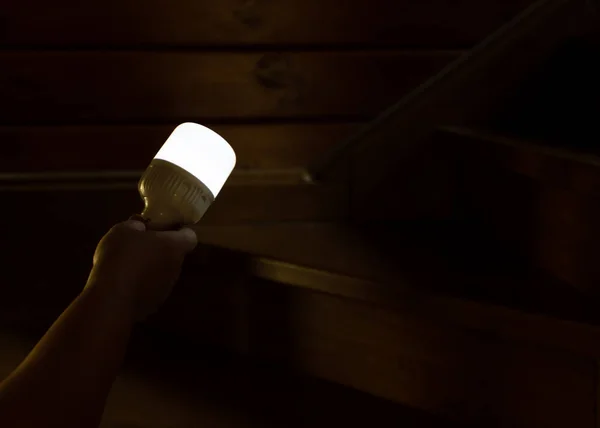 A womans hand holds a portable rechargeable LED emergency light with a built-in battery and illuminates the way up the stairs. Light source during blackout or at night. Dark shot