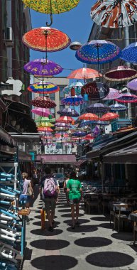 İstanbul, Türkiye - 19 Temmuz 2023: İstanbul 'un Asya yakasındaki büyük Kadıköy bölgesinde yer alan Umbrella Caddesi boyunca yürüyen insanlar. Yukarıda asılı renkli şemsiyeler.