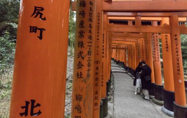 Kyoto, Japonya - 27 Aralık 2023: Parlak turuncu torii kapıları tarafından çerçevelenmiş patikanın yönlerini kontrol eden birkaç kişi. Fushimi Inari Tapınağı.