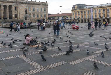 Bogota, Colombia - June 29, 2024: Plaza Bolivar is the main square of the Colombian capital Bogot. A woman sells corn to feed pigeons. The statue of Simon Bolivar is in the background. clipart