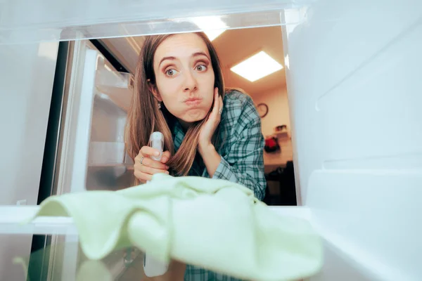 Stressed Girl Trying to Clean Her Fridge Using Detergent and Cloth