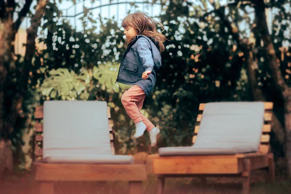 庭の小さな女の子のジャンプラウンジチェア屋外 — ストック写真