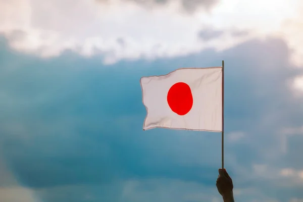 Hand Waving the Flag of Japan on a Beautiful Sunrise Sky
