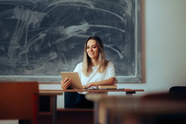 Masada oturan mutlu öğretmen bir bilgisayar tableti tutuyor. 
