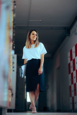 Okul koridorlarında yürüyen öğretmen elinde bir pano tutuyor.