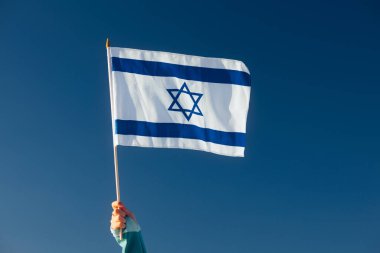 Hand Waiving an Israeli Flag on a Blue Sky  clipart