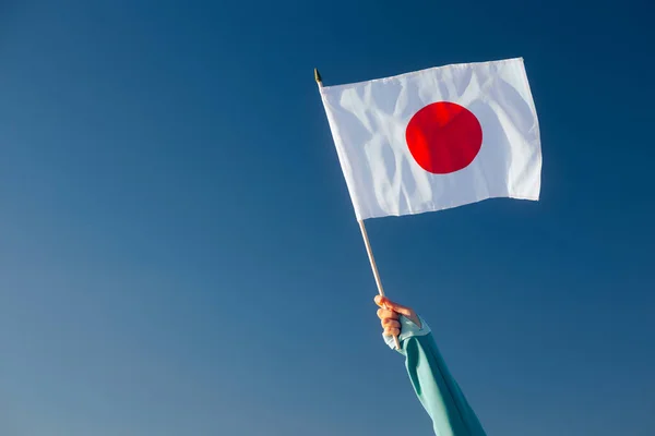 stock image Hand Waiving a Japanese Flag on a Blue Sky 