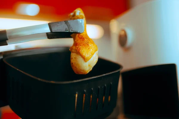 Kitchen tongs Holding an Air Fryer Healthy Chicken Drum Home cook taking out meat dish from air frying basket