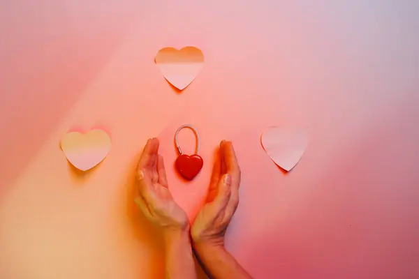 Hands Protecting a Heart Shaped Lock on a Pastel Background