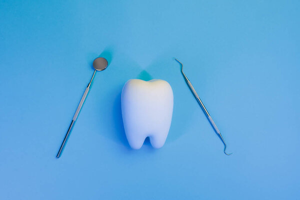 Tooth Next to a Dental Mirror and Probe on a Blue Background 