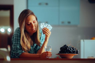 Kadın uyumadan önce bir bardak suyla haplarını alıyor.