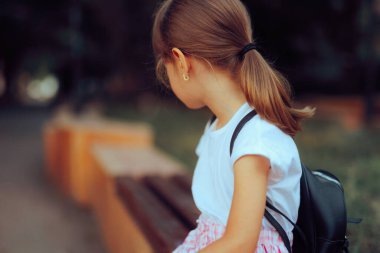 Açık bir bankta sırt çantası takan küçük bir kız. 