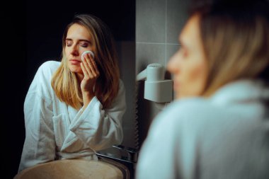 Tuvaletteki aynada pamuk pedlerle makyaj yapan kadın.