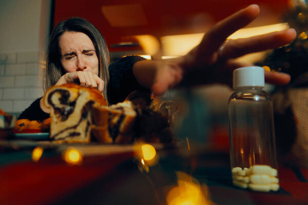 Женщина переедает на Рождество тянется за таблетками от боли в животе 
