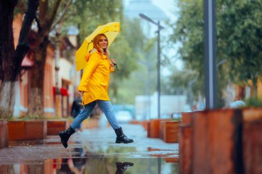 Su birikintilerinin üzerinden atlayan mutlu kadın yağmurun tadını çıkarıyor.