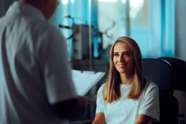 Doktor, tıbbi kabinede gülümseyen bir hastayla konuşuyor. 
