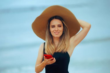 Büyük güneş şapkalı kadın akıllı telefonunu tutuyor.