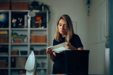 Kadın ütülemeden önce gömleğin yakasını kontrol ediyor.