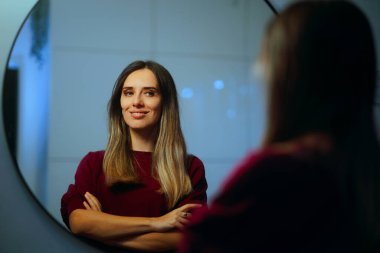 Mutlu Kadın, aynada kendine güvenle gülümsüyor.